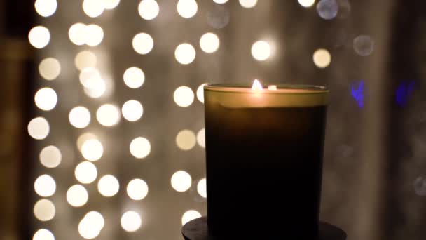 Bright parofin candle in glass burns at night on background of gerlands lights — Video Stock