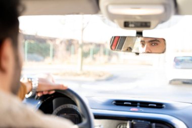 Man holding driving wheel riding car looking in rearview mirror at daytime