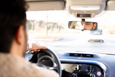 Man holding driving wheel riding car looking in rearview mirror at daytime