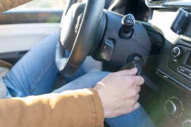 Man casually dressed with hands holding driving wheel starting engine with key