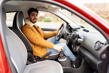 Eastern man in jacket holding driving wheel and manual gear box riding car