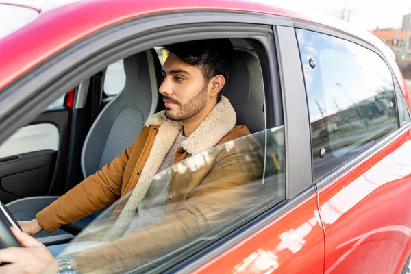 Man in jacket holding driving wheel riding car at daytime. View from outside