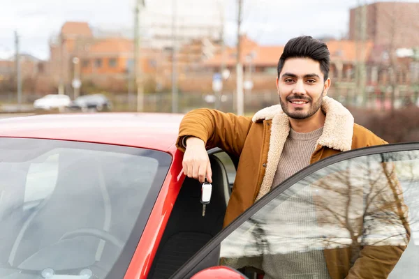 Hombre latino o árabe cerca de coche con llaves con puerta abierta en la ranura de estacionamiento de la ciudad Fotos de stock
