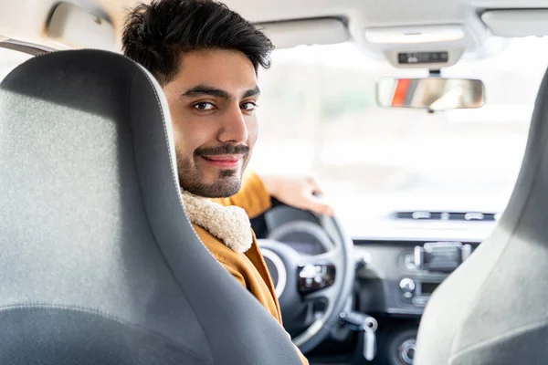 Hombre vestido casualmente con la mano en el volante mirando en el asiento trasero en la cámara Fotos de stock libres de derechos