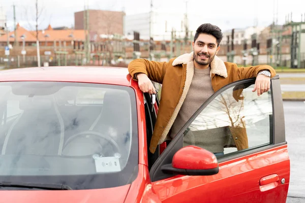 Hombre latino o árabe cerca de coche con llaves con puerta abierta en la ranura de estacionamiento de la ciudad Imagen de stock