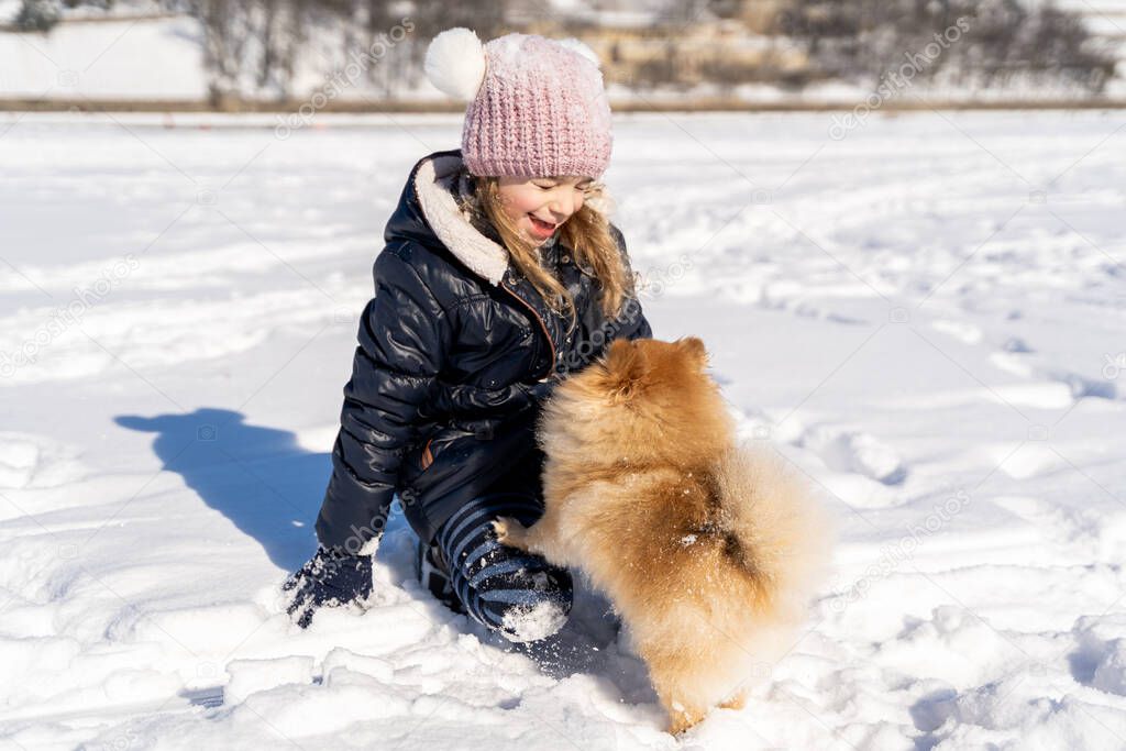 Little girl in warm clothes training and speaking with dog pet Spitz on snow