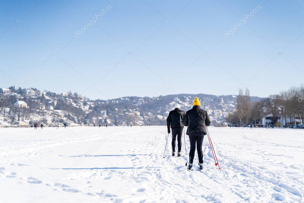Two elderly athletes in sporty clothes skiing across field covered with snow