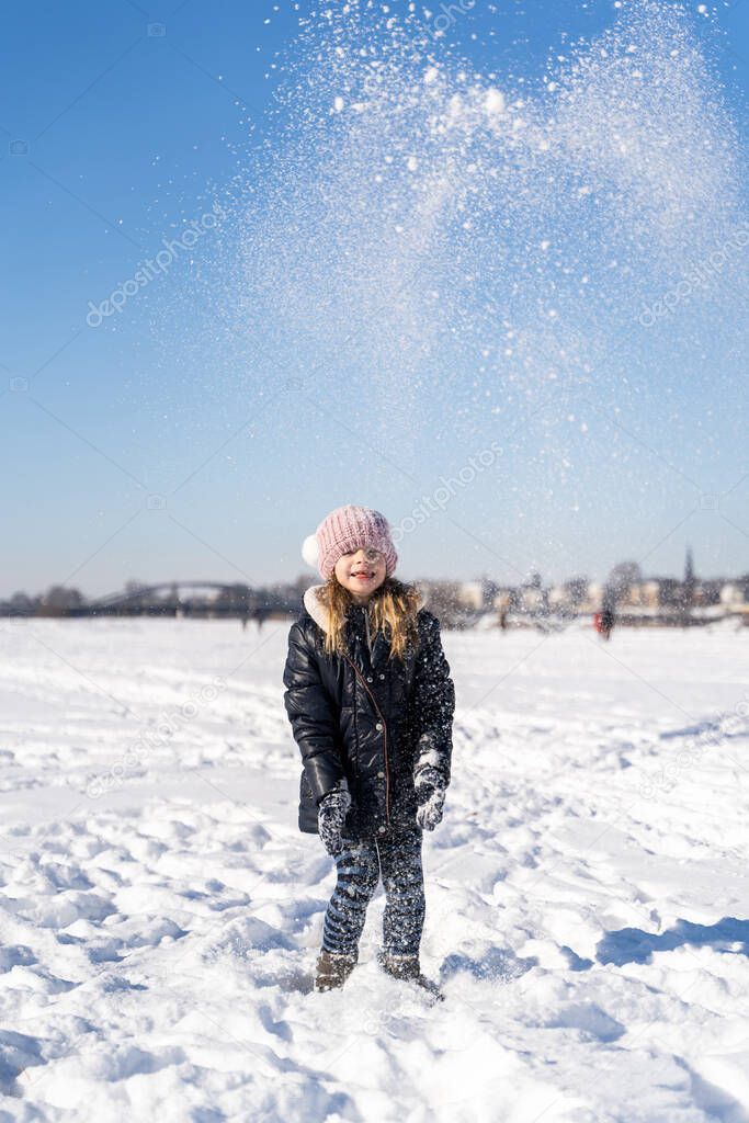 Young smiling preschool girl playing with snow outside on sunny winter weather