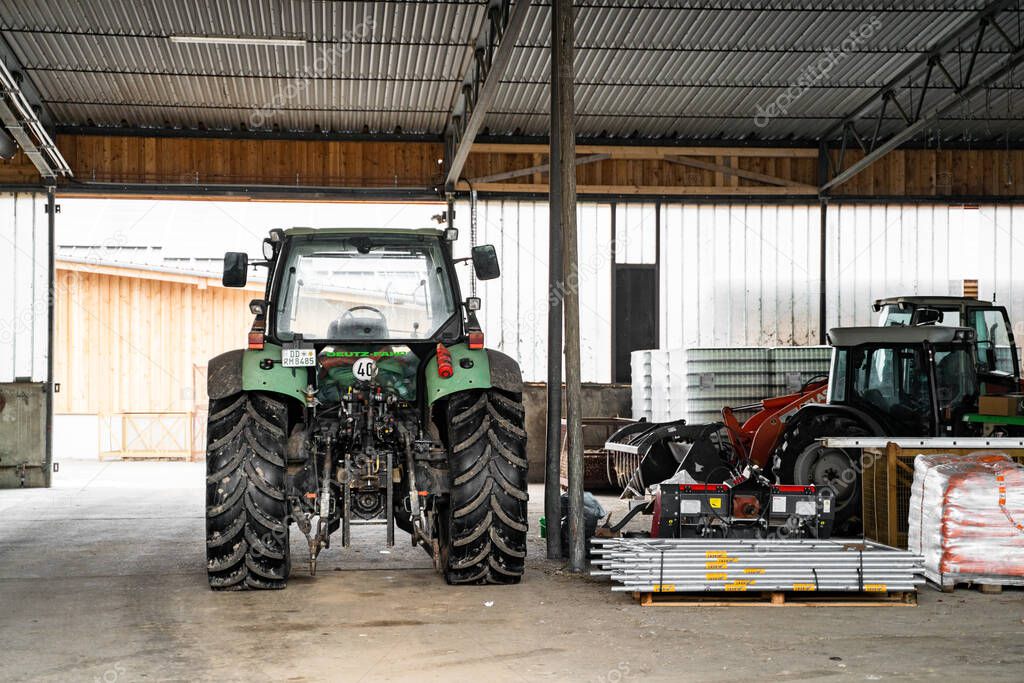 Green tractor with big wheels in garage near agricultural fixtures at daytime