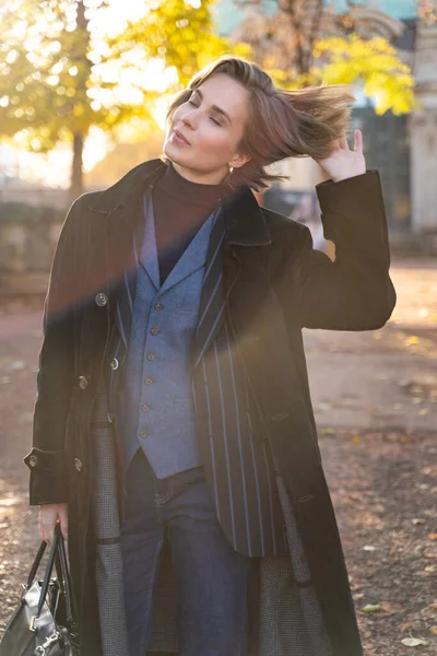 Молодая блондинка в полосатой куртке, джинсах и жилете касается волос — стоковое фото