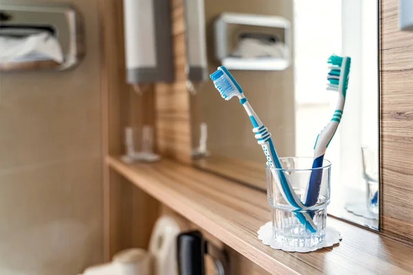 Two bright toothbrushes in glass cup in bathroom with mirror and window in hotel — Stock Photo, Image
