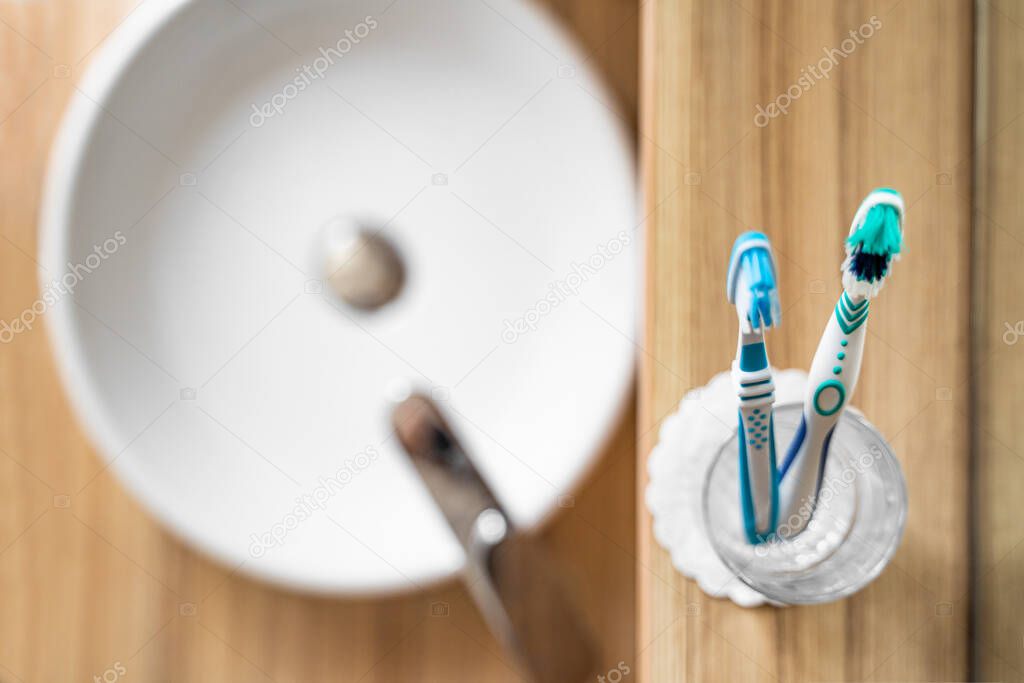 Two bright toothbrushes in glass cup in bathroom near sink and faucet in hotel
