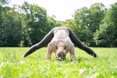 Aerobik yapan, antrenmandan sonra esneyen ya da yazın güneşli bir parkta yeşil çim çayırında pilates yapan sıradan spor kıyafetleri giyen Asyalı ya da beyaz genç bir kadın. Arka plan, yüz yok.
