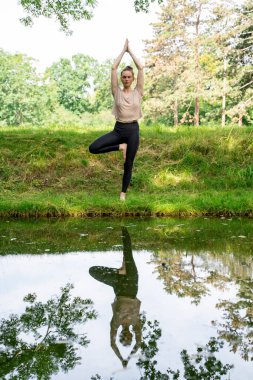 Spor kıyafetleri giymiş genç bir kadın yoga pozu veriyor. Elleri havada, meditasyondan sonraki gibi dua ediyor. Ya da yaz parkındaki göl kıyısında yeşil çimen kredisiyle pilates yapıyor. Ön görünüm