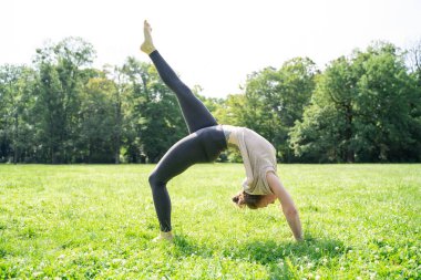 Spor kıyafetleri içinde, spor kıyafetleri içinde, sırt üstü şınav çeken, bacaklarıyla yoga tekeri pozu veren, antrenmandan sonra sırtını esneten ya da yaz güneşli parkta yeşil çimen kredisiyle pilates yapan beyaz bir kadın.