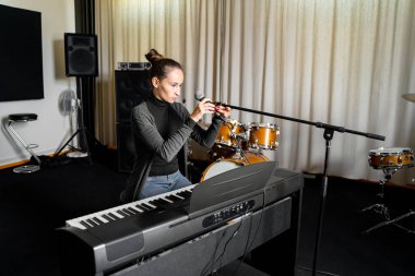 Genç Asyalı ya da Kafkas esmer kadın müzik stüdyosunda dijital klavye elektronik piyano çalıp şarkı söylemeye hazırlanan mikrofon ayarlıyor. Hobi, eğitim, hafta sonu aktiviteleri