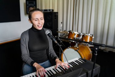 Genç Asyalı ya da Avrupalı esmer kadın, mikrofon ve yüksek sesle şarkı söyleyerek ve müzik stüdyosunda tek başına dijital klavye elektronik piyano çalarak eğleniyor. Sınavdan önce öğrenci öğrenmesi