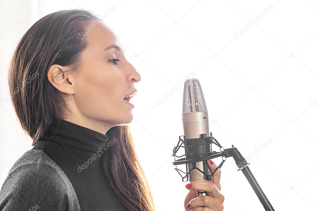 Young Asian or Caucasian brunette woman singing song to microphone alone in professional music studio. Radio host speaking to her listeners in broadcasting radio studio. Streaming podcast
