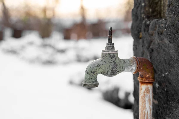 Old rusty retro outdoor garden faucet without valve stands outside in snowy garden or park near forest at sunset on snowy winter day. Season weather specific, hobby