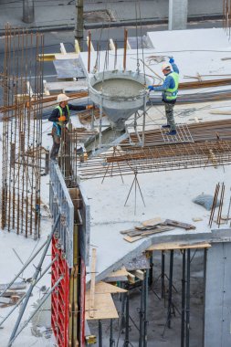 İnşaat alanı mavi gökyüzüne karşı çalışıyor. Hidrolik yelken yelkenli vinçleri ve temele beton dökülen işçileri kandırıyor. İnşaat alanındaki inşaat çalışmalarına çimento dökülüyor. 
