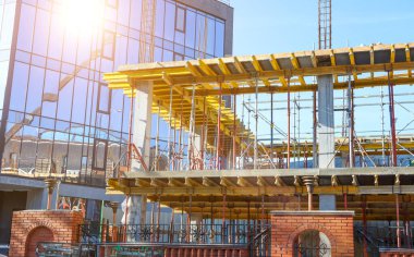 İnşaat alanı mavi gökyüzüne karşı çalışıyor. Hidrolik yelken yelkenli vinçleri ve temele beton dökülen işçileri kandırıyor. İnşaat alanındaki inşaat çalışmalarına çimento dökülüyor. 