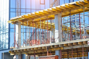 İnşaat alanı mavi gökyüzüne karşı çalışıyor. Hidrolik yelken yelkenli vinçleri ve temele beton dökülen işçileri kandırıyor. İnşaat alanındaki inşaat çalışmalarına çimento dökülüyor. 