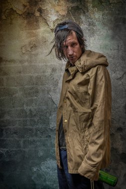 Keş adam yeşil anorak ve mavi eşofmanlı taş duvarın yanında