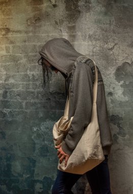 Gri kazaklı, tekstil çantalı ve kot pantolonlu bir erkek.