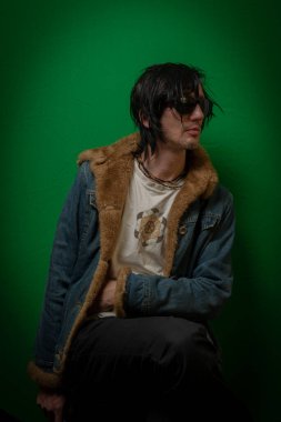 Koyu yeşil duvarın yanında oturan siyah saçlı adam.