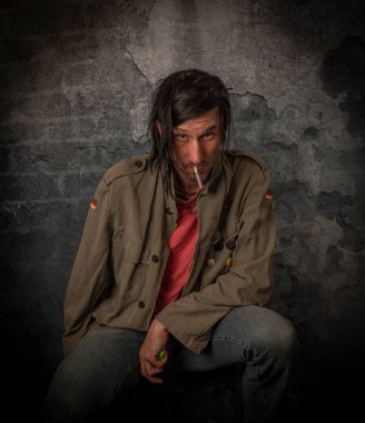 Esrarkeş adam, siyah saçlı ve şişeli, eski taş duvarın yanında.