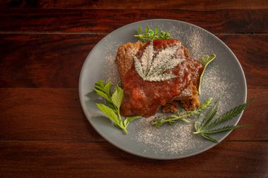 Şeker erikli marihuana ezmeli kek ve mavi tabakta şifalı otlar ve ahşap masa.