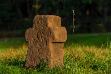 Krkonose dağları yakınlarındaki karanlık ormanın yakınındaki yeşil çayır üzerinde çok eski bir taş haç.