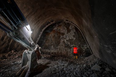 Yeraltı metro inşaatı. Kaya üzerinde turuncu yelek ve sert şapkalı bir adam (slate and quartzite) çalışmaktadır. Çek Cumhuriyeti 'nin Prag kentindeki geleceğin metro hattı 