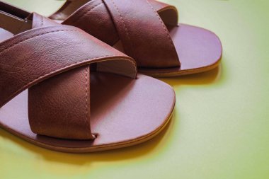 Kahverengi deri ayakkabıları kapat, kadınlar için sandaletler ve fotokopi alanı olan sarı bir arka plan.