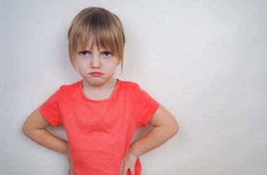 Beyaz arka planda pembe tişörtlü, sarı saçlı tatminsiz bir kız. 4 yaşında, şeytani görünüşlü, pembe tişörtlü bir kız. Aile sorunları kavramı, çocuk yetiştirme, anlaşmazlıklar.