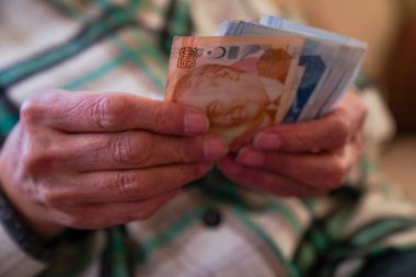 Kırışık ellerin Türk lira banknotlarını tuttuğu yakın plan.  