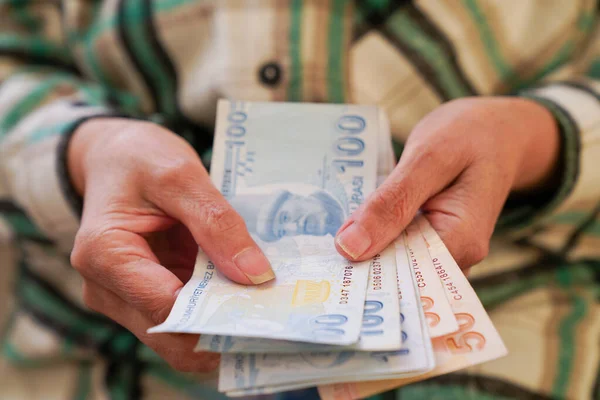 Kırışık ellerin Türk lira banknotlarını tuttuğu yakın plan.  