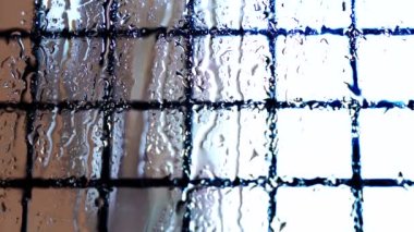 Pencere yüzeyinden akan yağmur damlaları. Dışarıda şiddetli yaz yağmuru var. Şiddetli rüzgar ve yağmur damlaları balkondaki cam pencereye düşüyor..