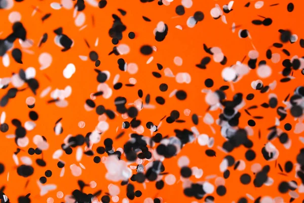Bílé černé konfety létají na oranžovém pozadí. Halloween party. — Stock fotografie