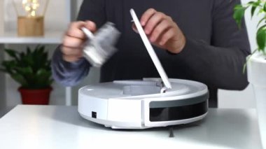 Bir adam, robot elektrik süpürgesine toz ve enkaz toplamak için bir filtre ve bir kap yerleştirir..