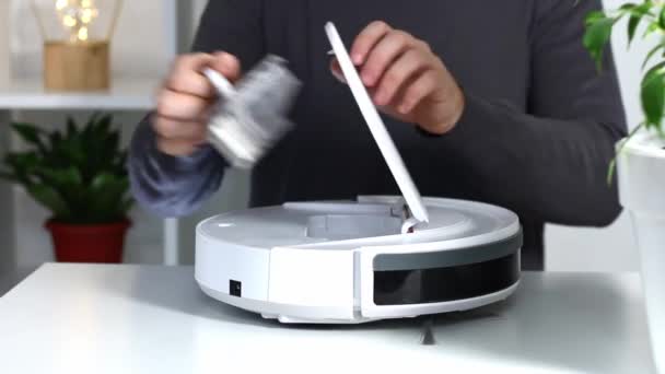 Un hombre inserta un filtro y un recipiente para recoger polvo y escombros en la aspiradora robot. — Vídeo de stock