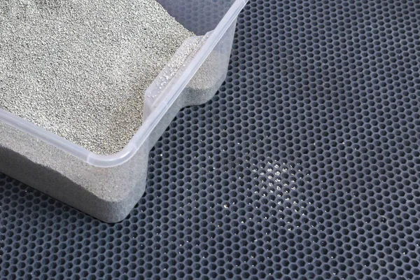 A litter box with clumping litter sits on a honeycomb EVA mat. Small filler particles from the feet