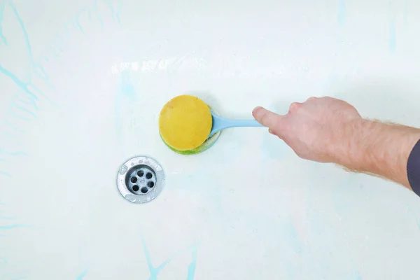 Um homem aplica um limpador de banho e esfrega banho com uma escova, pano. Limpeza do banheiro. — Fotografia de Stock