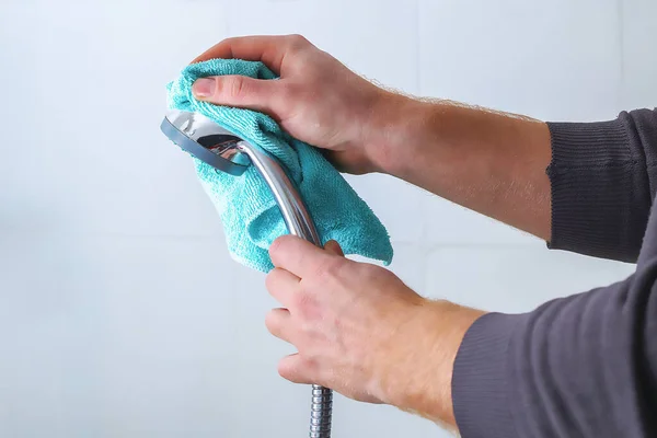 한 남자가 헝겊으로 샤워기 머리를 닦는다. 집안 청소, 화장실. — 스톡 사진