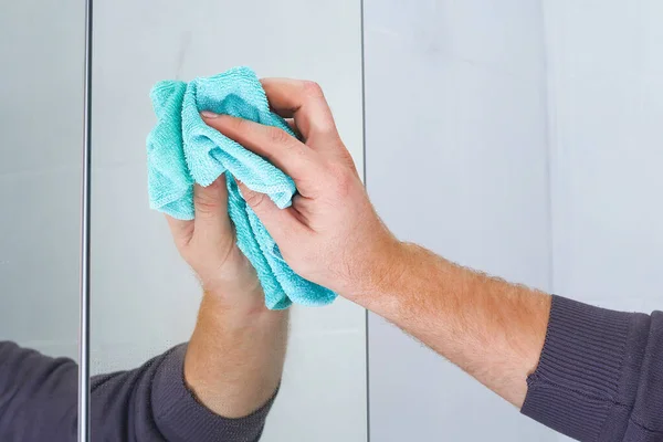 Um homem limpa um armário de espelhos na casa de banho com pano. Limpeza da casa, banheiro. — Fotografia de Stock