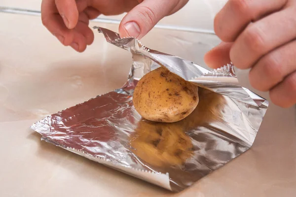 Человек заворачивает очищенный сырой картофель в фольгу и помещает их на вешалку проволоки, чтобы испечь их в духовке. — стоковое фото