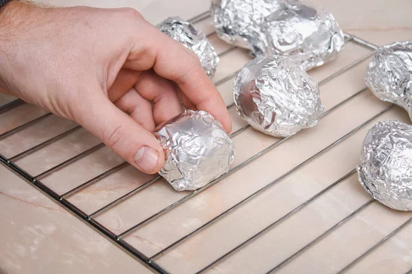 O homem envolve batatas cruas descascadas em papel alumínio e coloca-os no rack de arame para assá-los no forno. — Fotografia de Stock