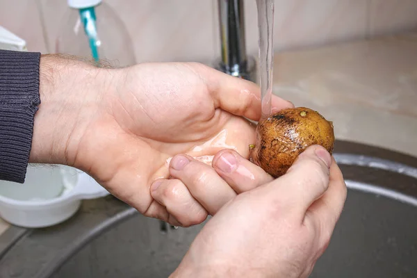 A man washes raw potatoes in sink under water to bake them in foil in the oven. — Fotografia de Stock