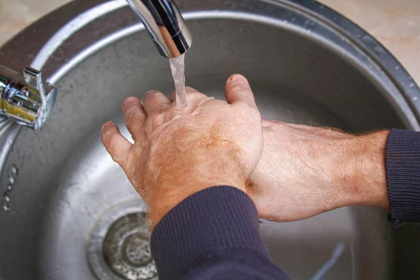 Мужчина моет руки с мылом в раковине на кухне после мытья картошки. — стоковое фото