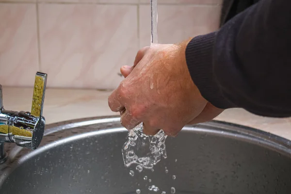 Un hombre se lava las manos con jabón en el fregadero de la cocina después de lavar papas. —  Fotos de Stock